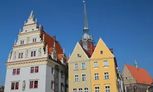 Kolorowe kamienice i wieża kościelna na rynku w Nysie pod błękitnym niebem.