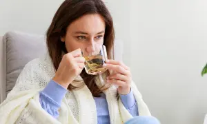 Kobieta pije napar z ziół, który może pomóc na biegunkę. Otulona kocem, szuka ulgi w domowym zaciszu.
