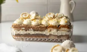 Ein Raffaello Tiramisu in einer Glasform, geschichtet mit Löffelbiskuits, Creme und Kokosraspeln. Obenauf dekorative Kokospralinen.