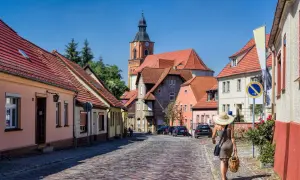 Idyllisches Dorf mit Kopfsteinpflasterstraße, Kirche und einer Frau mit Hut. Perfekt für Ausflugsziele Berlin Brandenburg.