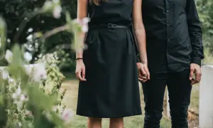 Ein Paar in schwarzer Kleidung, die Frau in einem schlichten Kleid, hält Händchen. Passende **Beerdigung Kleidung Frau Sommer** für einen traurigen Anlass.