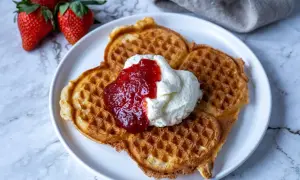 Belgiska våfflor med vispad grädde och jordgubbssylt, serverade med färska jordgubbar. En perfekt fika!