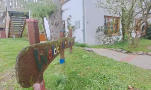 Holzschild "Waldorfkindergarten" vor einem Gebäude mit Spielturm. Mögliche Nachteile: wenig Struktur, viel Freiheit.