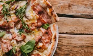 Kremowa pizza carbonara z boczkiem i rukolą na drewnianym stole.