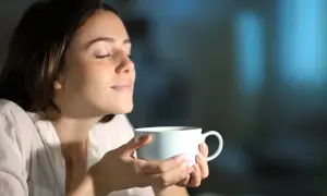Kobieta z zamkniętymi oczami wdycha aromat napoju. Może to być kawa lub napar z ziół na pobudzenie.