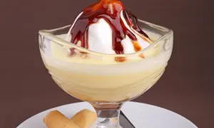 Un dessert crémeux avec une meringue nappée de caramel, servi dans un verre, évoquant des iles flottantes. Des biscuits fins l'accompagnent.