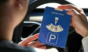 Person hält eine Parkscheibe mit der Aufschrift "Ankunftszeit" und dem Parkplatzsymbol.