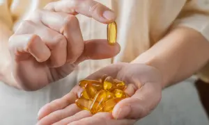 Dłoń trzyma kapsułkę z omega-3, zarejestrowaną jako lek. W drugiej dłoni garść takich tabletek.