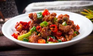 Chrupiący kurczak po kantońsku z papryczkami chili i zieloną cebulką na białym talerzu.