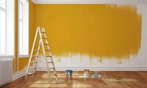 Drabina i puszki z farbą przy ścianie częściowo pomalowanej na żółto.