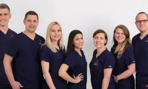 Grupa uśmiechniętych dentystów w granatowych uniformach na białym tle.