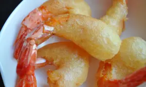 Plusieurs beignets de crevette dorés et croustillants, avec des queues de crevettes roses qui dépassent, servis dans une assiette blanche.