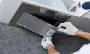 Ręce w białych rękawiczkach montują metalowy filtr okapu podszafkowego.