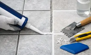 Application d'un joint carrelage silicone ou ciment avec un pistolet. Outils de pose à proximité.