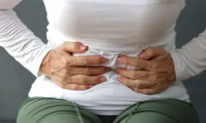 Dłońmi obejmuje brzuch, szukając ulgi. Zastanawia się, jaki błonnik na zaparcia będzie najlepszy.