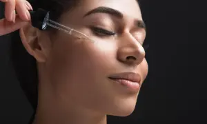 Una mano applica un siero viso con contagocce, forse contenente acido azelaico e retinolo, su una donna con gli occhi chiusi.
