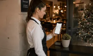Cameriera controlla sul telefono quanto viene pagata la domenica, mentre sullo sfondo si intravede un ristorante addobbato per Natale.