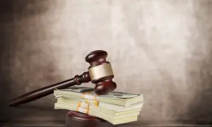 Młotek sędziowski na stosie banknotów dolarowych symbolizuje sprawiedliwość i finansową kompensatę.