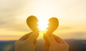 Mani che tengono due pezzi di un cuore spezzato contro un tramonto dorato. Un sentimento di nostalgia, non riesco a lasciarti andare.