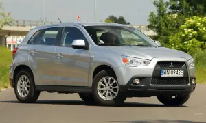 Srebrny Mitsubishi ASX 1.6 benzyna z kierowcą za kierownicą, zaparkowany na drodze z zielenią w tle.