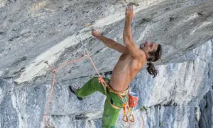 Alexander Huber klettert an einer steilen Felswand, sein Körper angespannt, die Hände greifen nach kleinen Vorsprüngen.