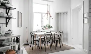En ljus och mysig matplats med ett träbord, svarta stolar och en vacker blomsterbukett. En taklampa i trä ger ett varmt sken.