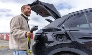 Man laddar sin soc elbil utomhus. En gul laddkabel hänger från bilen.