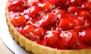 Una deliziosa torta di fragole, con fragole fresche e succose ricoperte da una lucida glassa rossa, su una base dorata.