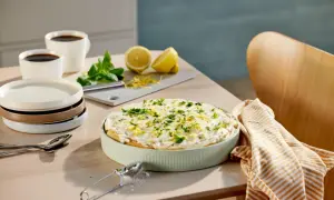 En krämig tiramisu limoncello, garnerad med citronzest och persilja, står på ett bord med kaffe och citroner.