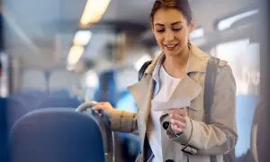 Kobieta w płaszczu trzyma bilet w pociągu, patrząc na niego z uśmiechem.