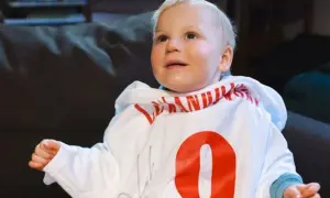 Uśmiechnięty chłopiec z zespołem Angelmana w białej bluzie z czerwonym napisem i cyfrą 9.