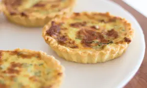 Trois petites quiches sans œuf dorées sur une assiette blanche. La pâte est croustillante et la garniture semble crémeuse.