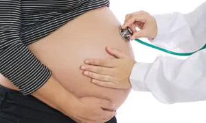 Une sage-femme utilise un stéthoscope pour le monitoring d'un ventre de femme enceinte.