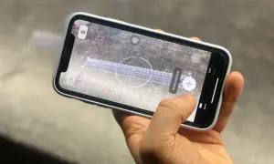 Dłoń trzyma telefon z włączoną aplikacją miarka. Na ekranie widoczna jest wirtualna linijka i przycisk "Dodaj prostokąt".