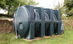 Grand réservoir de gasoil vert, posé sur une base en béton dans l'herbe. Une jauge indique le niveau, suggérant une longue durée de vie du gasoil.