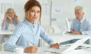 Kobieta w biurze, pracująca przy laptopie. Jej kod zawodu to księgowa, która skrupulatnie wypełnia dokumenty.