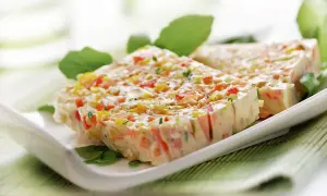 Tranches de terrine de légumes colorée, garnie de feuilles vertes, sur une assiette blanche.