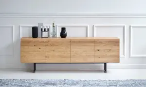 Ett stilrent sideboard i ljust trä med svarta ben, dekorerat med vaser och ljusstakar.