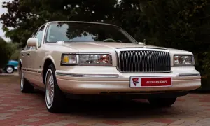 Beżowy Lincoln Town Car, przyszły youngtimer, lśni na tle zieleni. Klasyczna elegancja, która wciąż zachwyca.