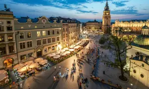 Wieczorny gwar na Rynku Głównym w Krakowie. Ludzie spacerują, siedzą w ogródkach kawiarnianych. W tle Sukiennice i wieża ratuszowa. To serce miasta, jego **sarbinowo centrum**.