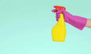 En hand i lila handske håller en gul sprayflaska med röd spraymunstycke, redo för en snabb dry clean.