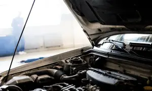Bilmotor med öppen huv. En person står i bakgrunden, kanske en mekaniker som undersöker igensatt luftfilter symtom.