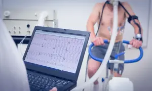 Un homme subit un test d'effort cardiologue sur un vélo d'appartement, avec un électrocardiogramme affiché sur un écran d'ordinateur.