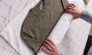 Hände rollen einen braunen Kaschmirpullover auf einem weißen Handtuch auf, um ihn nach dem Kaschmir waschen zu trocknen.