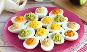 Assortiment d'œufs mimosa colorés sur une assiette rose. Des garnitures vertes, jaunes et orangées apportent une touche festive.