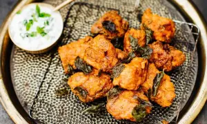 Knusprige chicken pakora, garniert mit frischen Kräutern, auf einem Gitterrost serviert. Daneben eine Schale mit Joghurt-Dip.