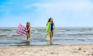 Zwei Mädchen rennen lachend mit Luftmatratzen über den mecklenburgische Seenplatte strand ins Wasser.