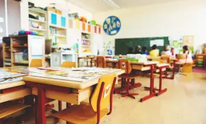 Helle, freundliche klassenraumgestaltung grundschule mit bunten Regalen, kindgerechten Tischen und Stühlen. Kinder sitzen im Hintergrund.