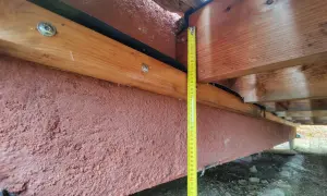Mesure de la hauteur d'une poutre en bois extérieur, avec un revêtement rouge pour sa protection.