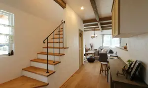 Un acogedor aseo bajo escalera con escalones de madera y barandilla negra. La sala de estar rústica se abre al fondo.